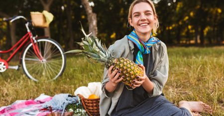 Joyful Girl Sitting On Picnic Blanket On Grass Happily Holding P Joyful Girl Sitting On Picnic Blanket On Grass Happily Holding P